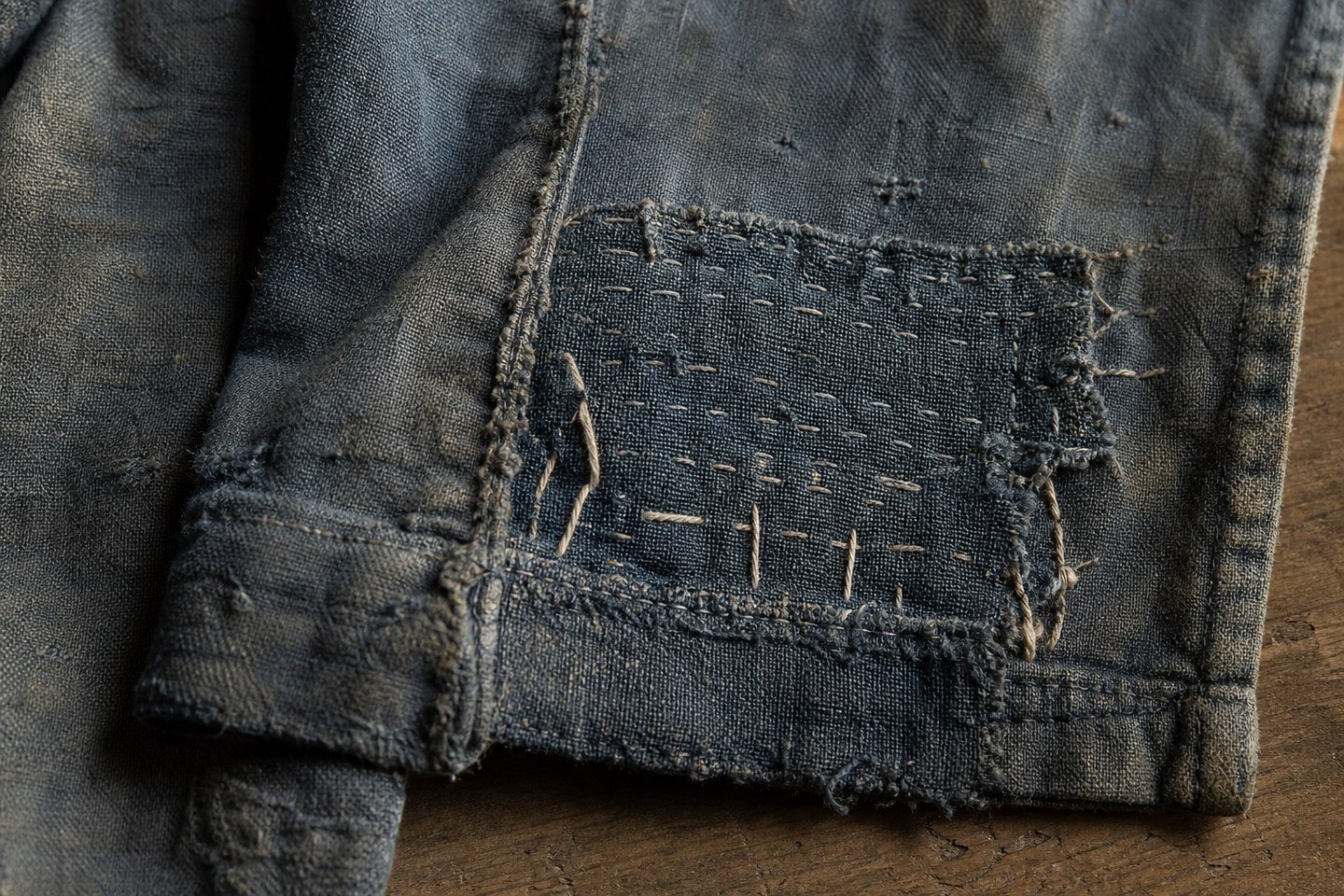 Close view of a frayed and carefully repaired section of an old work garment