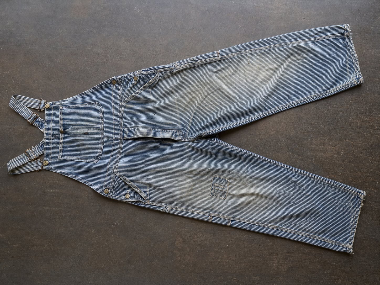 Worn blue-and-white striped work overalls laid flat for inspection