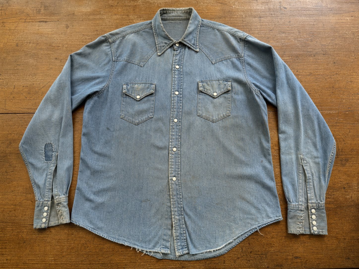 Faded blue Western snap shirt laid flat on a wooden inspection table